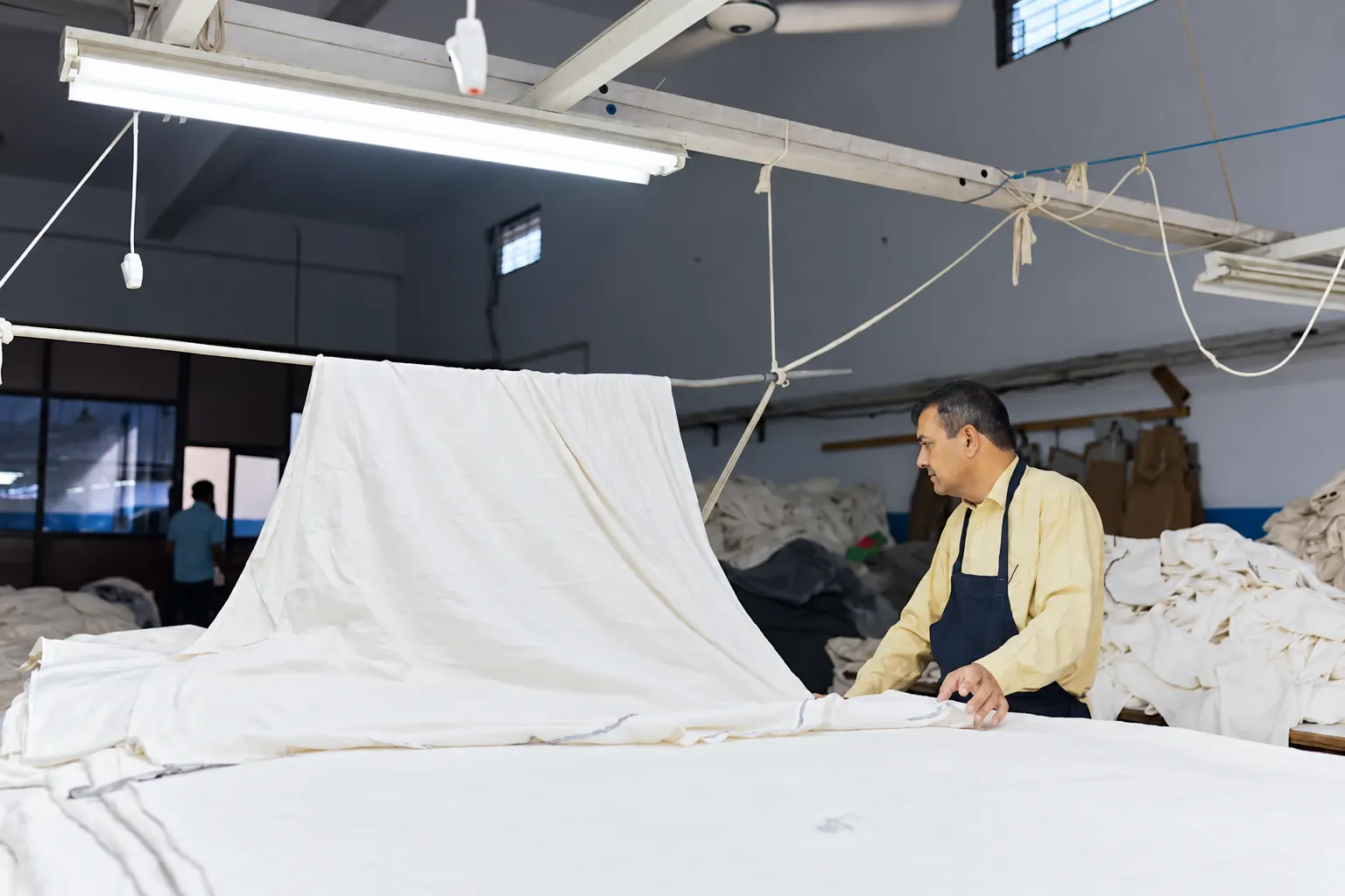 Fabric inspection & preparation Worker inspecting white fabric at a textile preparation table.